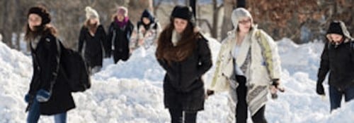 Students in winter coats walking through the snow to class.