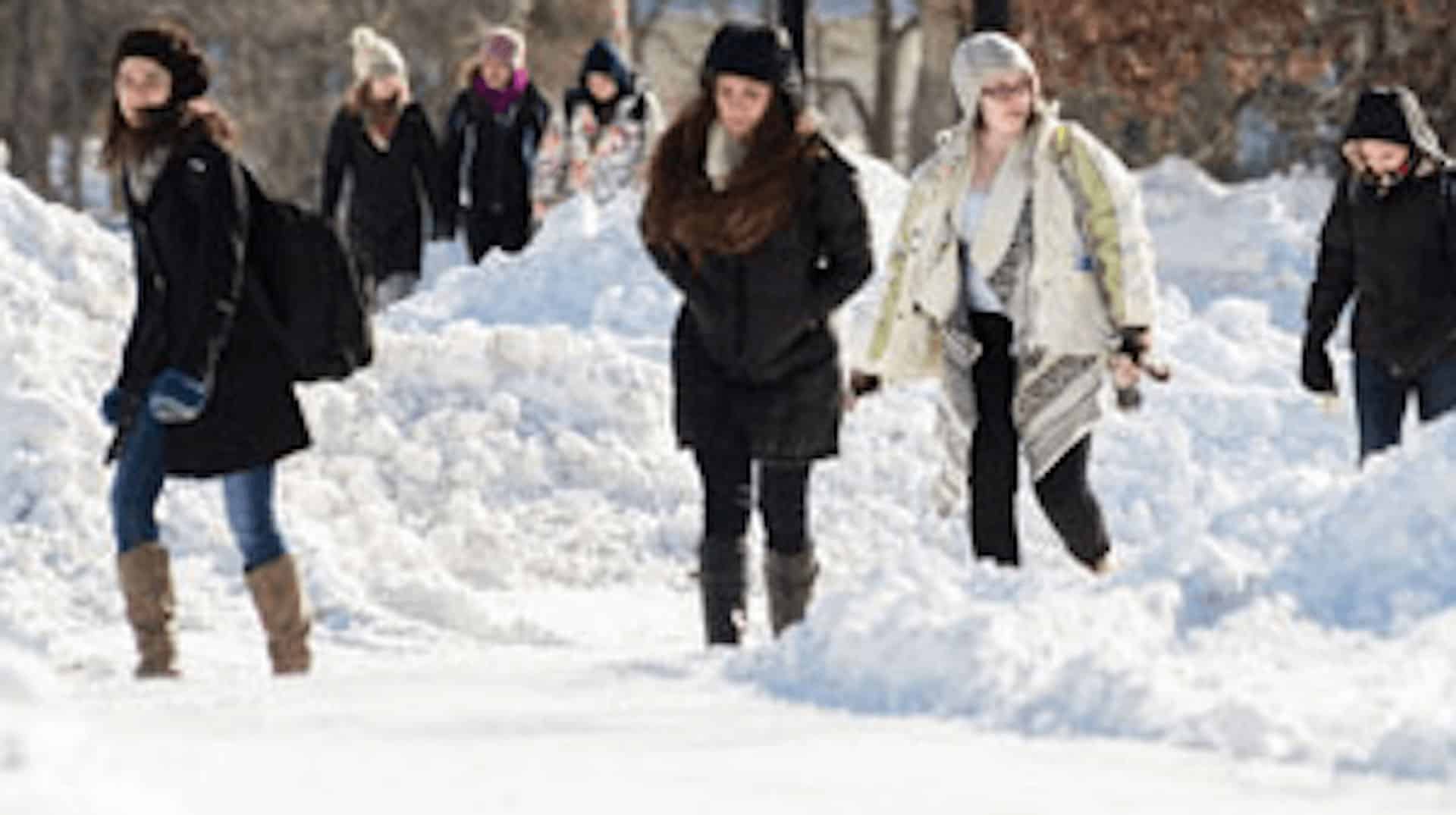 Students in winter coats walking through the snow to class.