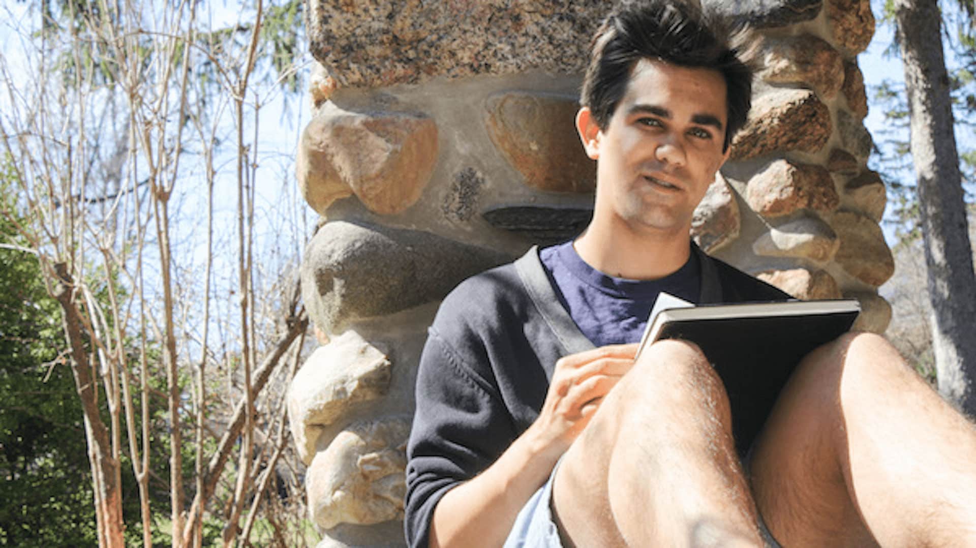 Aaron Schepps sitting against a rock wall.