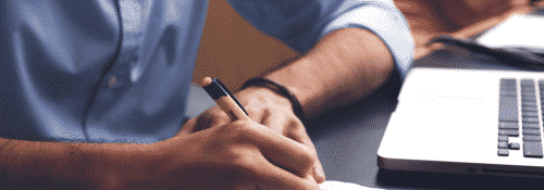 Student writing a list in front of their computer.