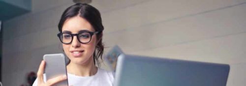 stock photo of girl looking at phone in front of laptop