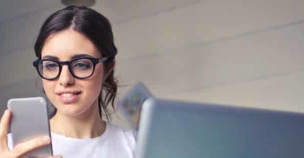 stock photo of girl looking at phone in front of laptop