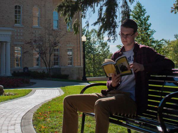 Student reading a book on a bench on campus.