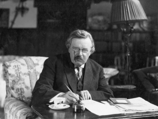 G. K. Chesterton writing at his desk.