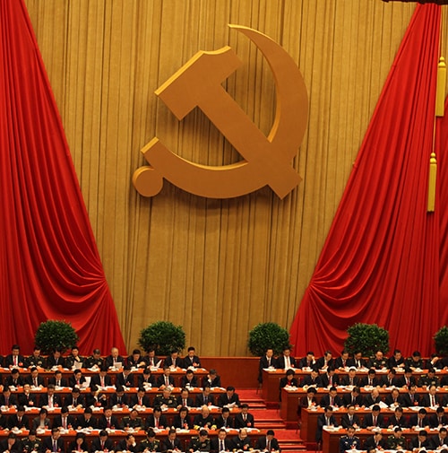 Rows of seated Chinese politicians with the Hammer and Sickle displayed on the back wall.