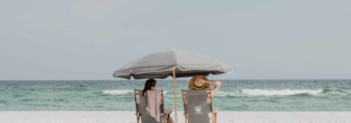 Two women sitting under a canopy on the beach.