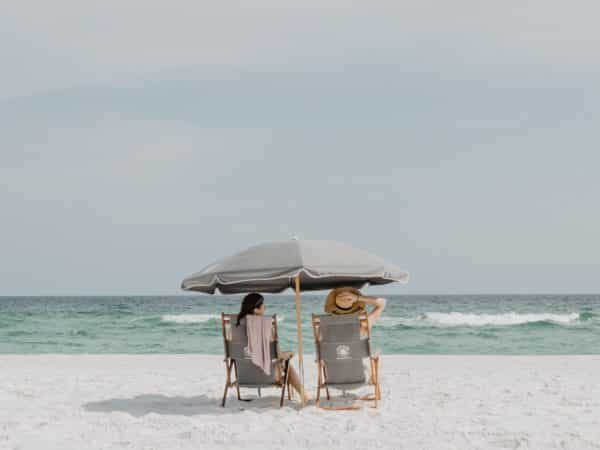 Two women sitting under a canopy on the beach.