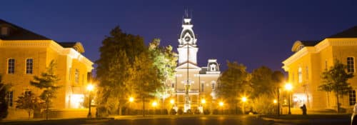 Wide view of Hillsdale College Central Hall at night with sidewalk lamps on.
