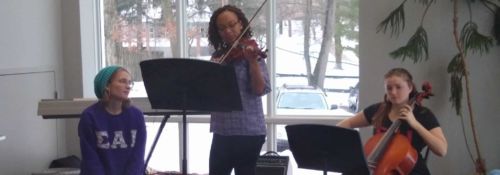 Three female students play instruments for a small audience