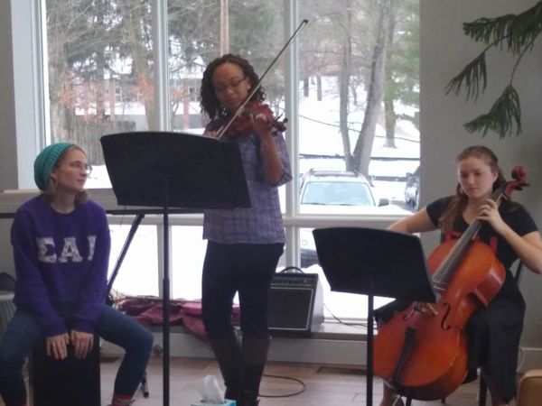 Three female students play instruments for a small audience