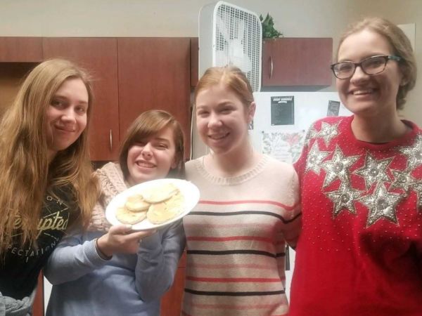Four female students stand in a dorm kitchen with a plate of homemade tortillas