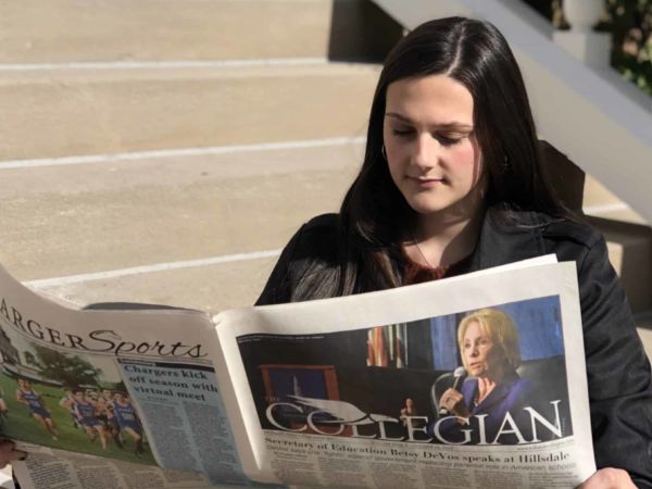 Students sits on Central Hall front steps, reading The Collegian