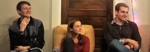 Three college students sit in separate chairs in a living room