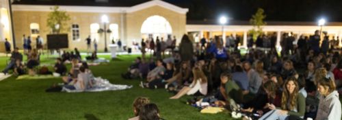 students lay on a blanket on the middle of a grassy quad at night