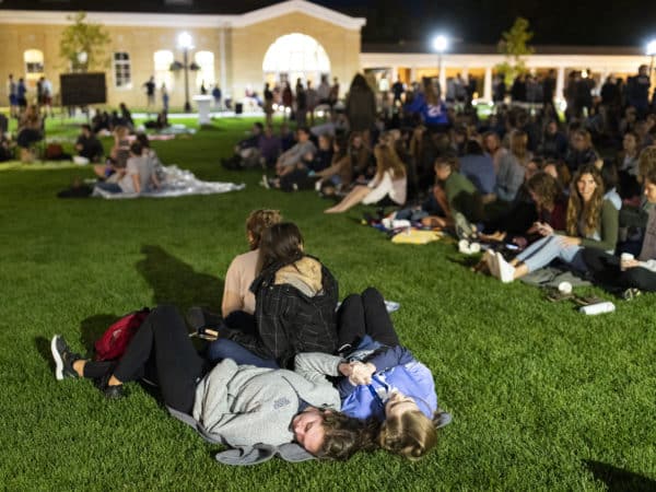 students lay on a blanket on the middle of a grassy quad at night