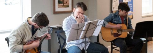 three male students sitting, playing acoustic music in a coffee house