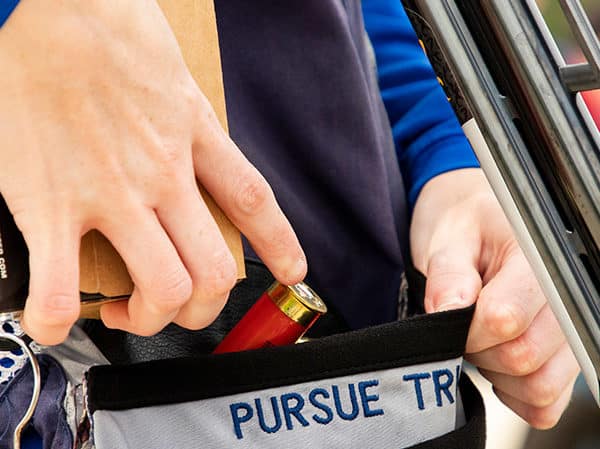 A competitve shooter reaches for shotgun shells in her ammunition pouch.