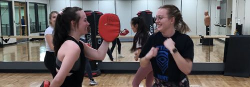 Two women in a gym studio holding targets and wearing boxing gloves