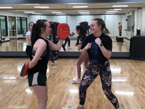 Two women in a gym studio holding targets and wearing boxing gloves