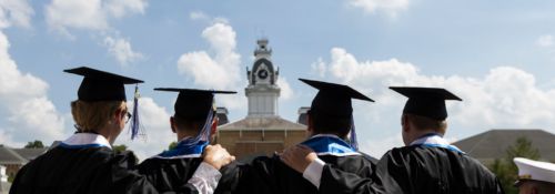 graduating students facing clocktower with blue skies