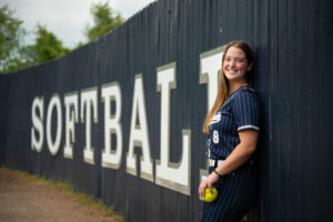 Photo of woman standing against a wall that reads Softball